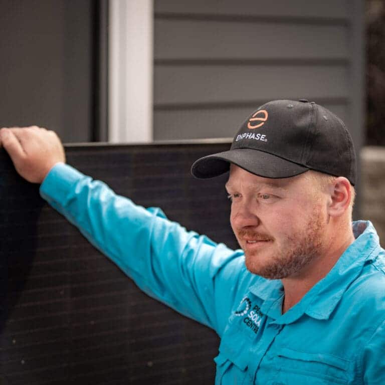 A man with a hat leaning against a solar panel.