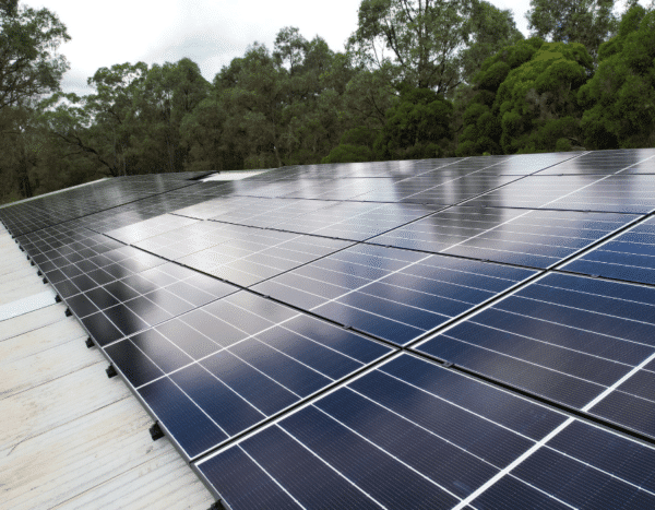 Large array of solar panels installed on a roof, surrounded by trees under a cloudy sky.
