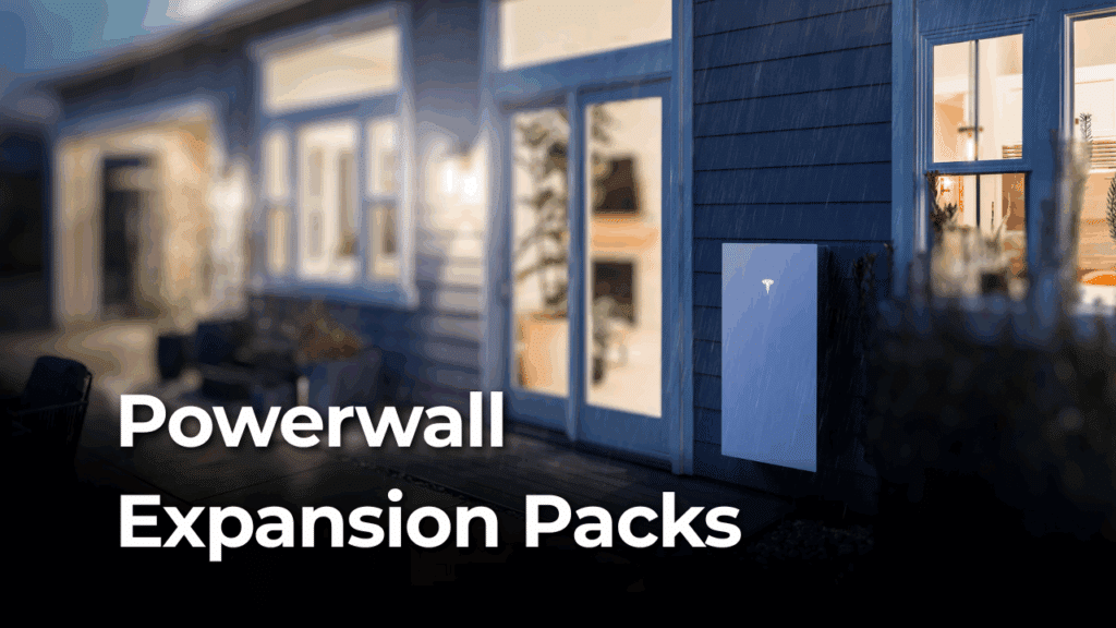 A Tesla Powerwall is mounted on the exterior wall of a modern house at dusk, with text reading "Powerwall Expansion Packs.