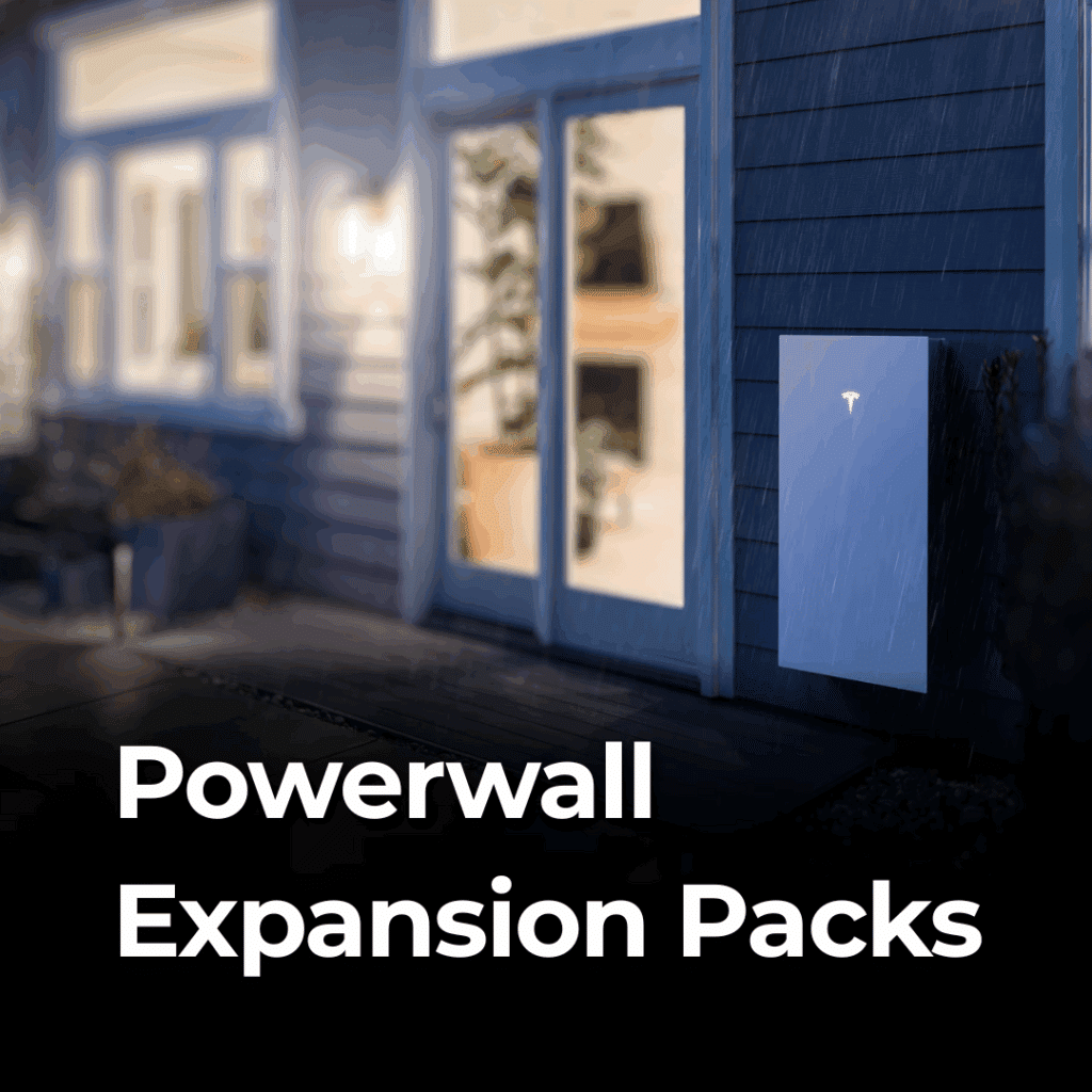 A Tesla Powerwall is mounted on the exterior wall of a house at night, next to large windows. The words "Powerwall Expansion Packs" are displayed at the bottom.
